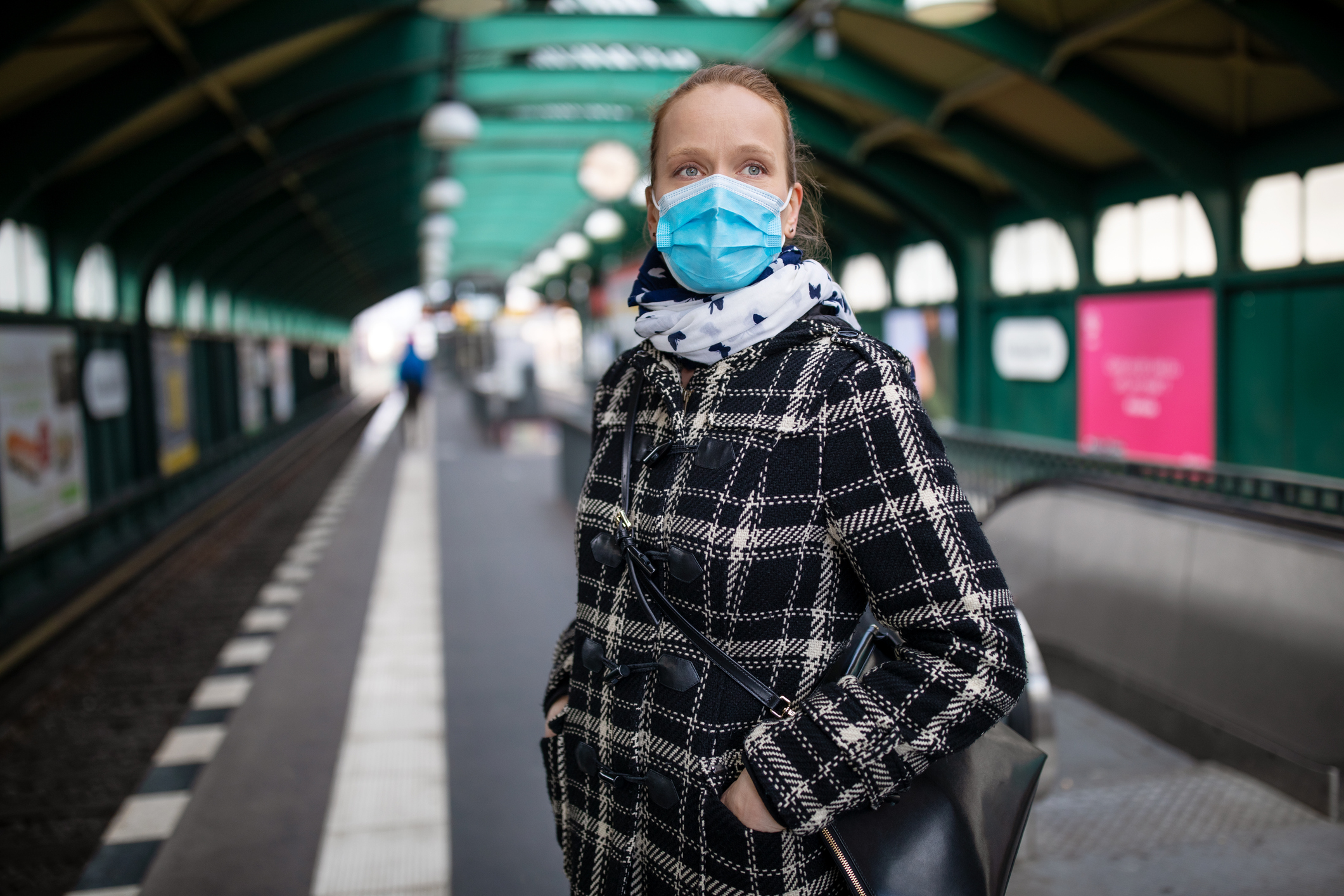 Woman in winter coat with protective mask on face standing on metro station. Female commuter waiting for the train during Covid-19 outbreak.